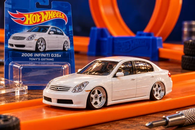 A fictional toy-car concept of Tony’s white 2006 Infiniti G35x, displayed on orange track beside miniature-car packaging.