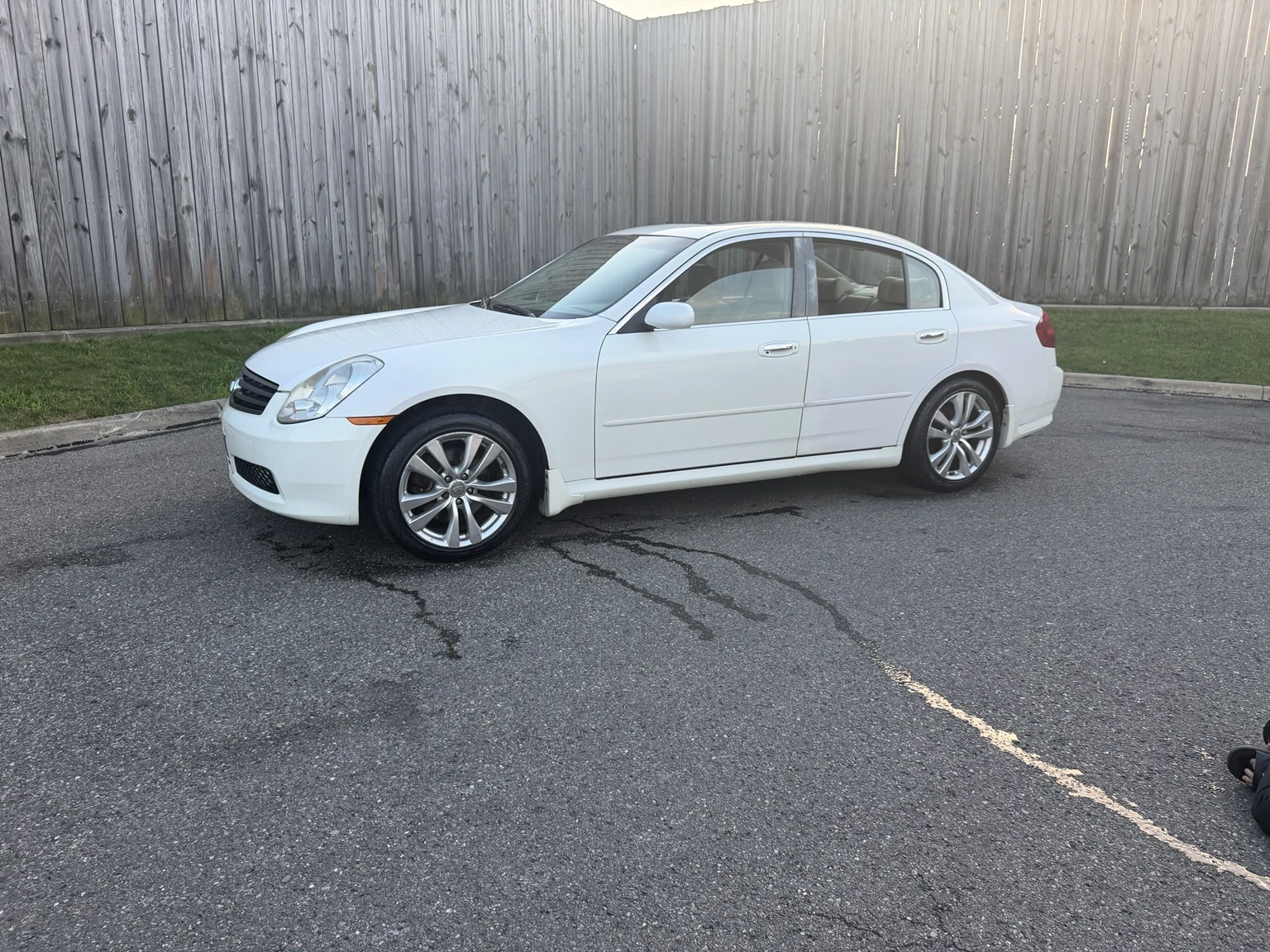 Actual front three-quarter view of Tony’s white sedan with its original wheels beside a wooden fence.